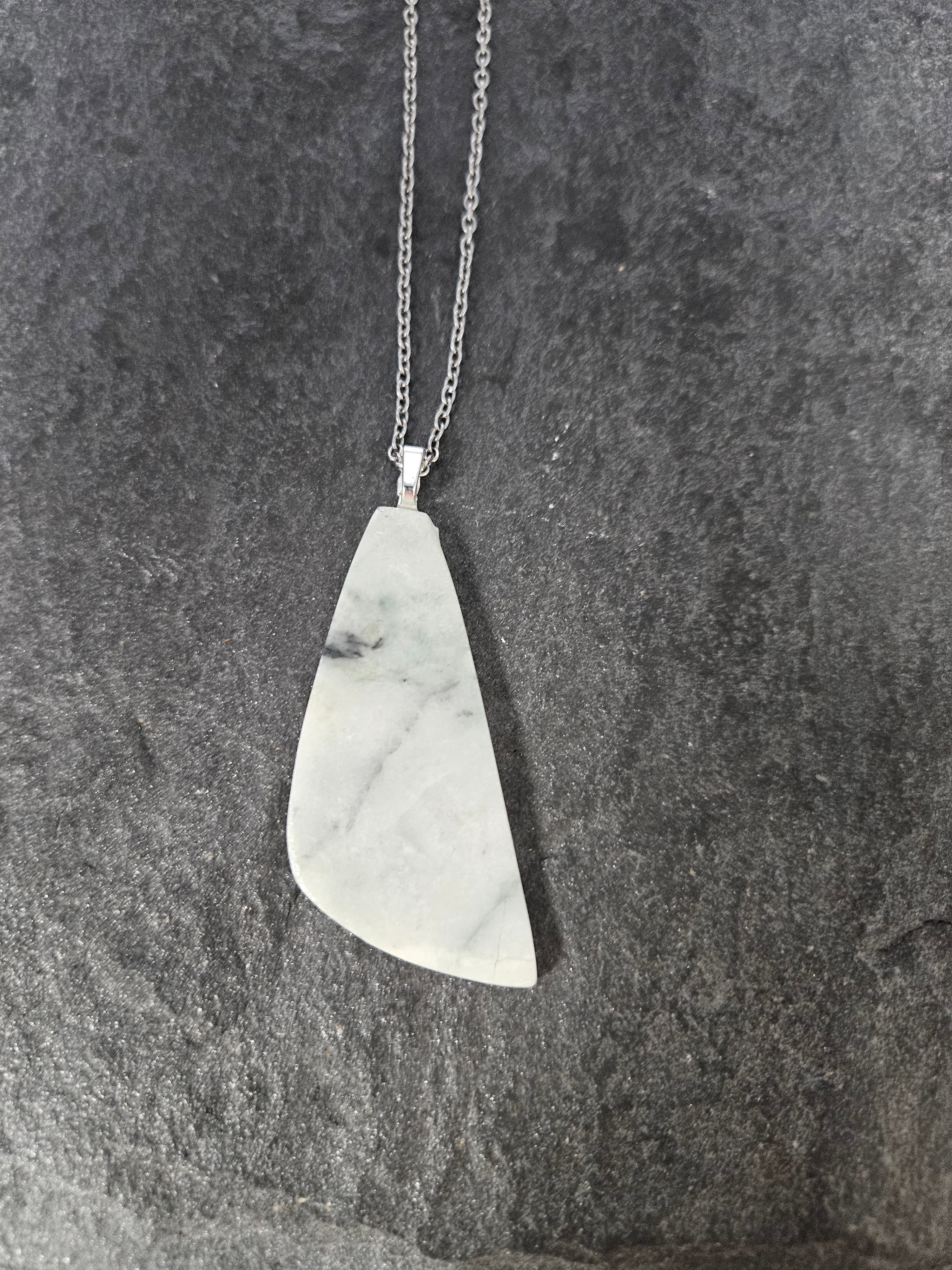 A silver pendant necklace featuring a polished, irregularly shaped white stone with gray veining, displayed on a dark textured slate surface.