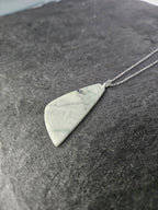 A silver necklace with a polished, irregular triangular pendant made of light gray and white marbled stone, resting on a dark textured surface.
