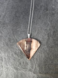 A silver chain necklace with a triangular pendant made from a polished wood slice showing natural brown and beige grain, displayed on a dark gray slate surface.