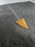 A triangular pendant made of natural brown wood or bone with visible grain, hanging from a silver chain against a dark textured background.