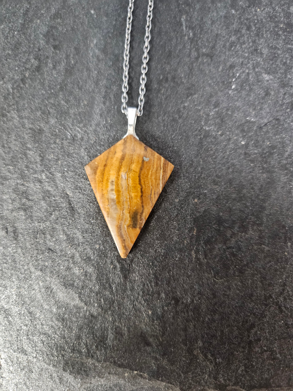 A triangular wooden pendant necklace with a silver-toned chain, displayed on a dark textured gray background.
