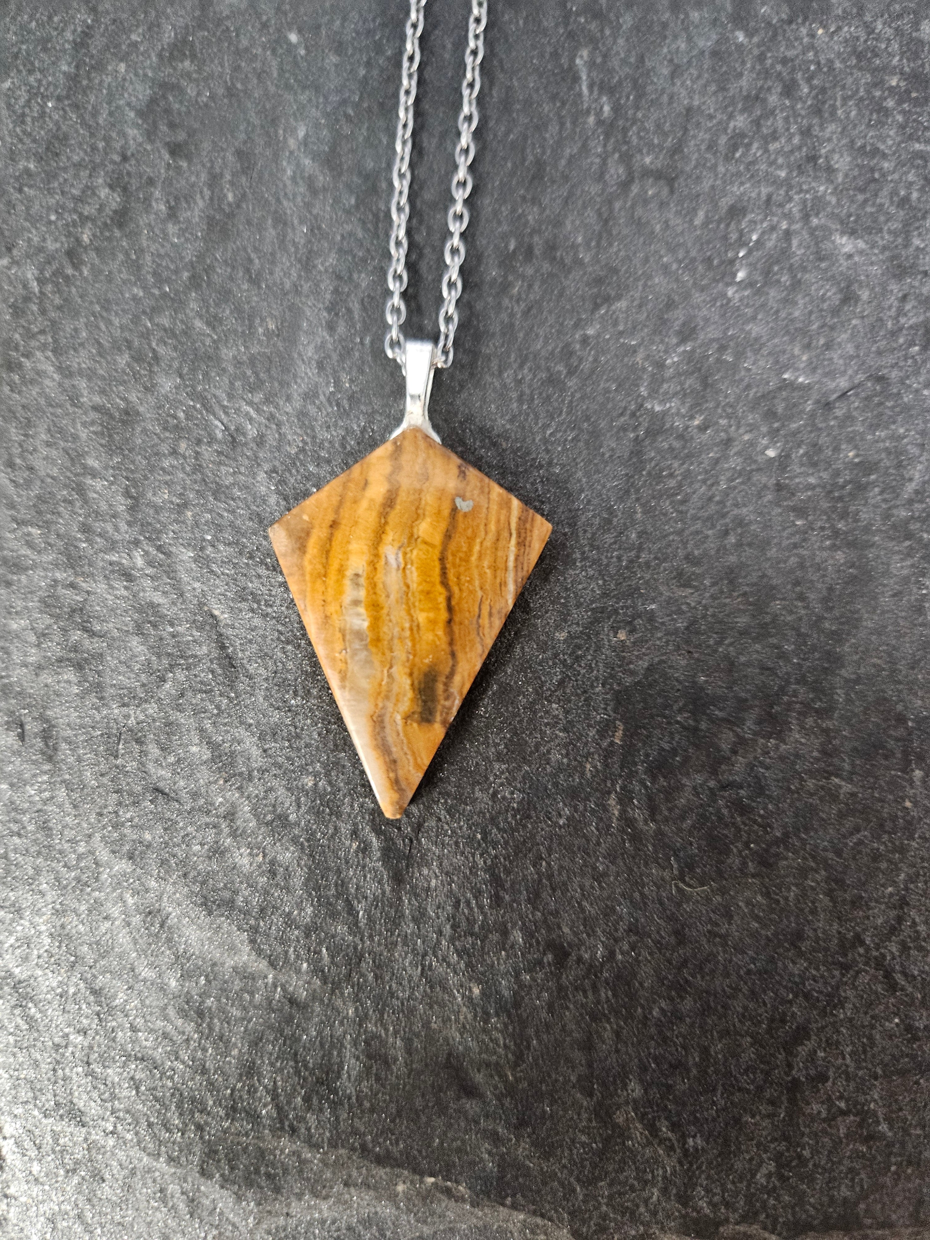 A triangular wooden pendant necklace with a silver-toned chain, displayed on a dark textured gray background.